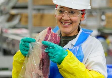 Female JBS employee packing meat.  Smiling at camera