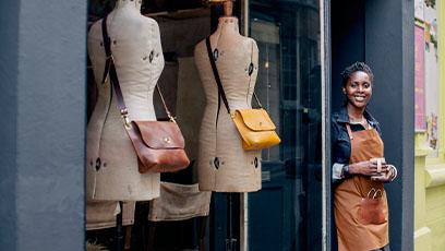 A female entrepreneur stands outside her designer women's shop, with a cup of coffee.