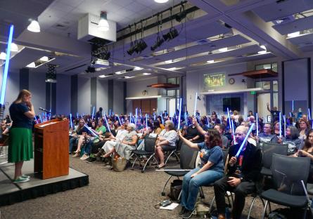 Attendees raise their lightsabers in response to a question.