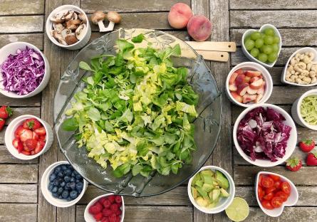 A salad surrounded by bowls of fruit and chopped vegetables