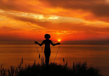 Someone standing in front of the sea at sunset who's about to jump rope