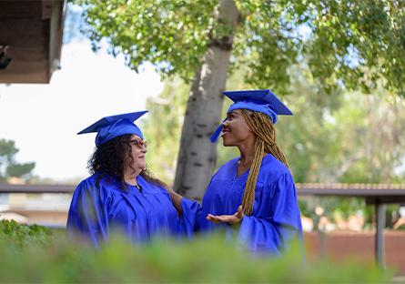 two female graduates smiling at each other during a commencement ceremony