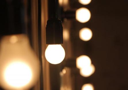 A lit lightbulb suspended in front of a vanity mirror