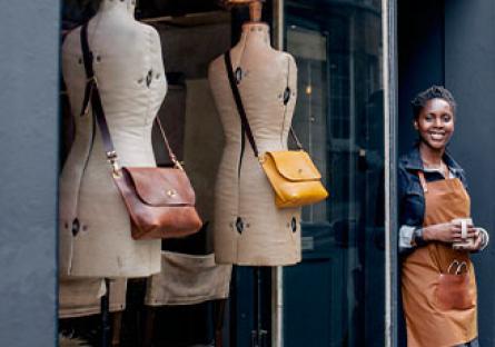 A female entrepreneur stands outside her designer women's shop, with a cup of coffee.